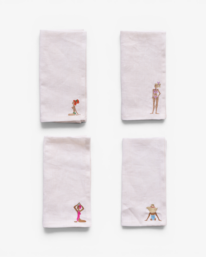 Four white napkins with embroidered designs on a white background