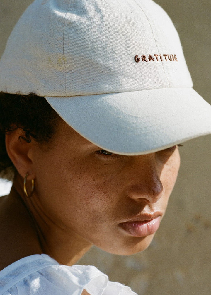 Person wearing a white cap with 'GRATITUDE' text against a neutral background