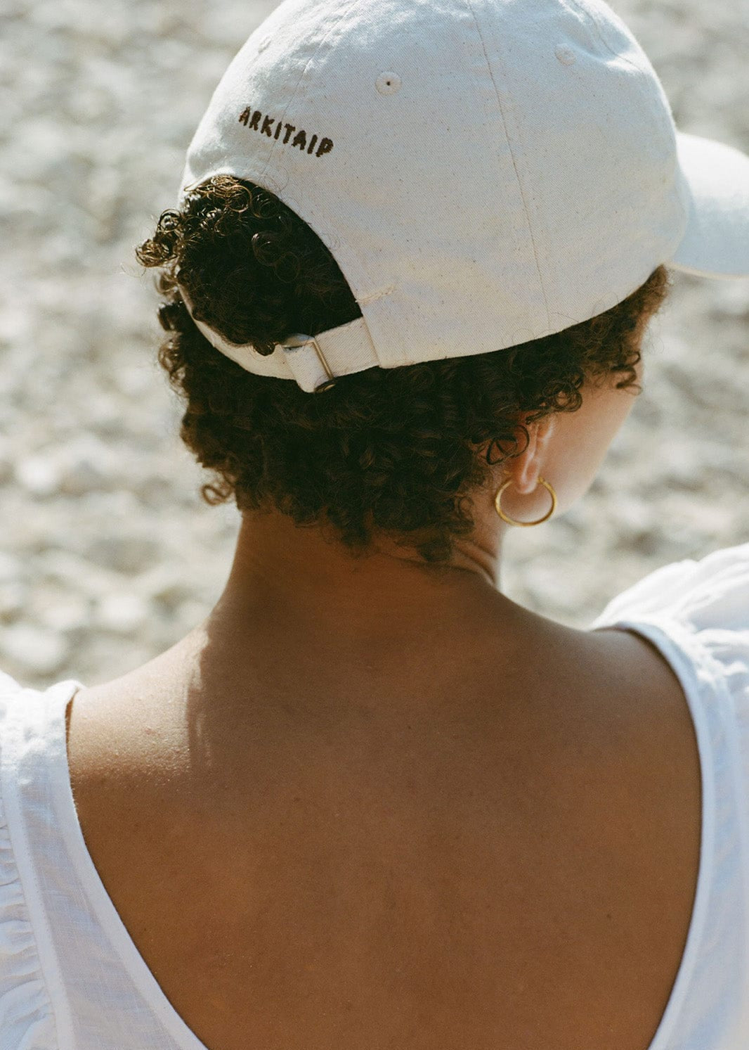 Person wearing a white cap with 'ARKITAIP' branding on a blurred natural background
