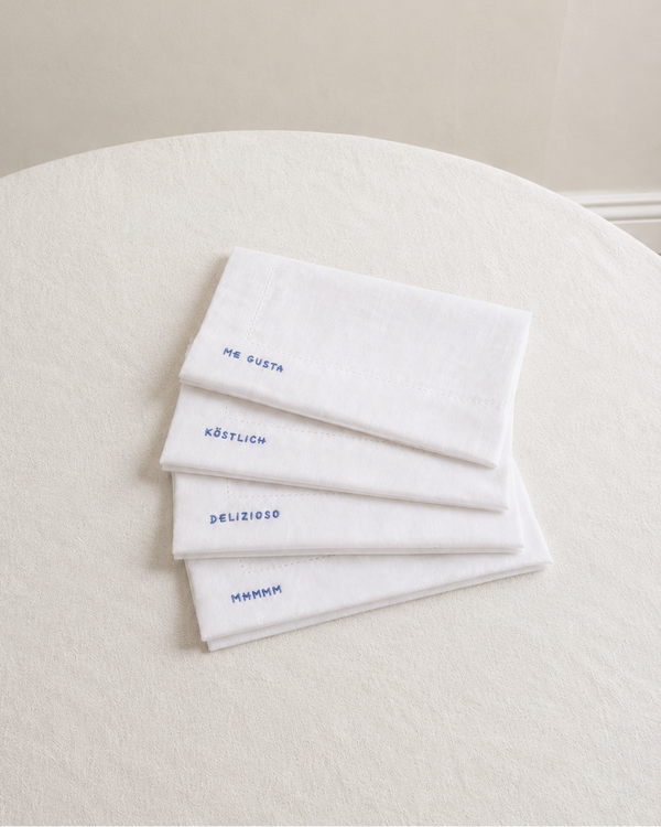 Four white napkins with embroidered text on a white surface