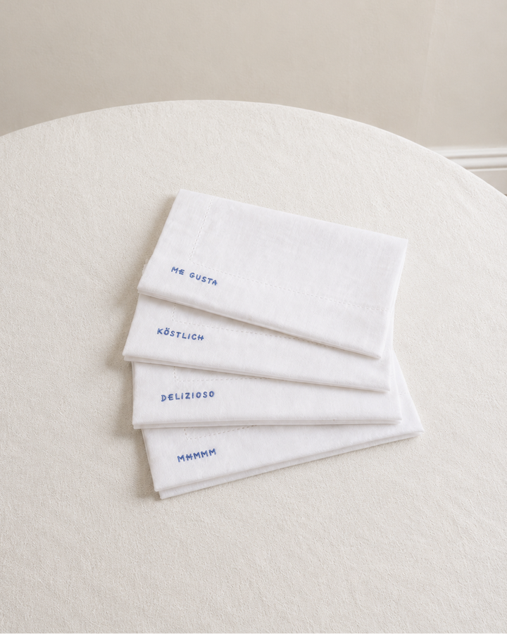 Four white napkins with embroidered text on a white surface