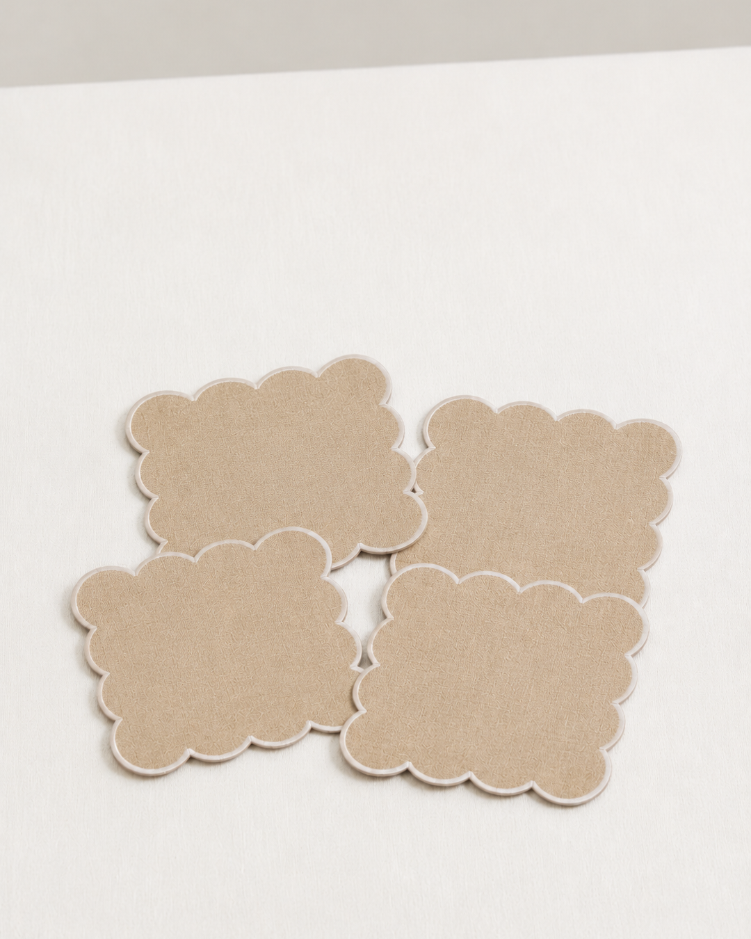 Four beige linen napkins with scalloped edges on a white surface