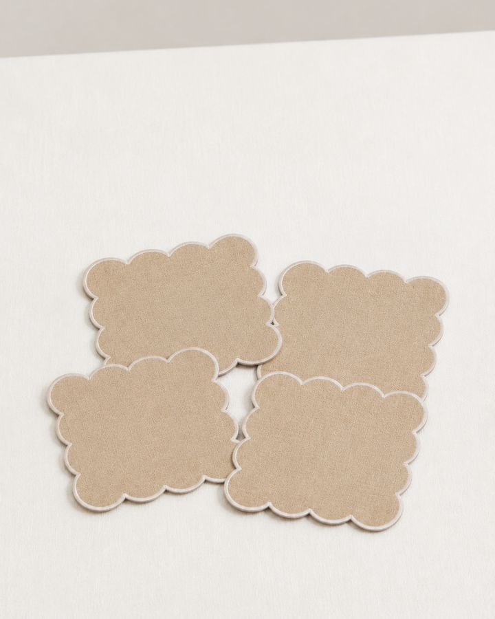 Four beige linen napkins with scalloped edges on a white surface