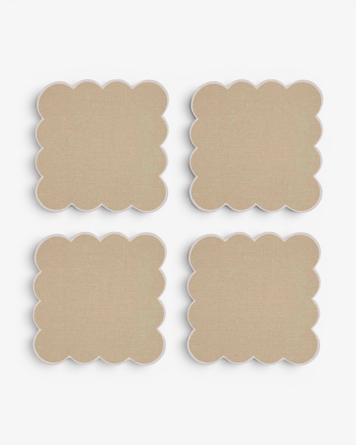 Four beige square coasters with scalloped edges on a white background