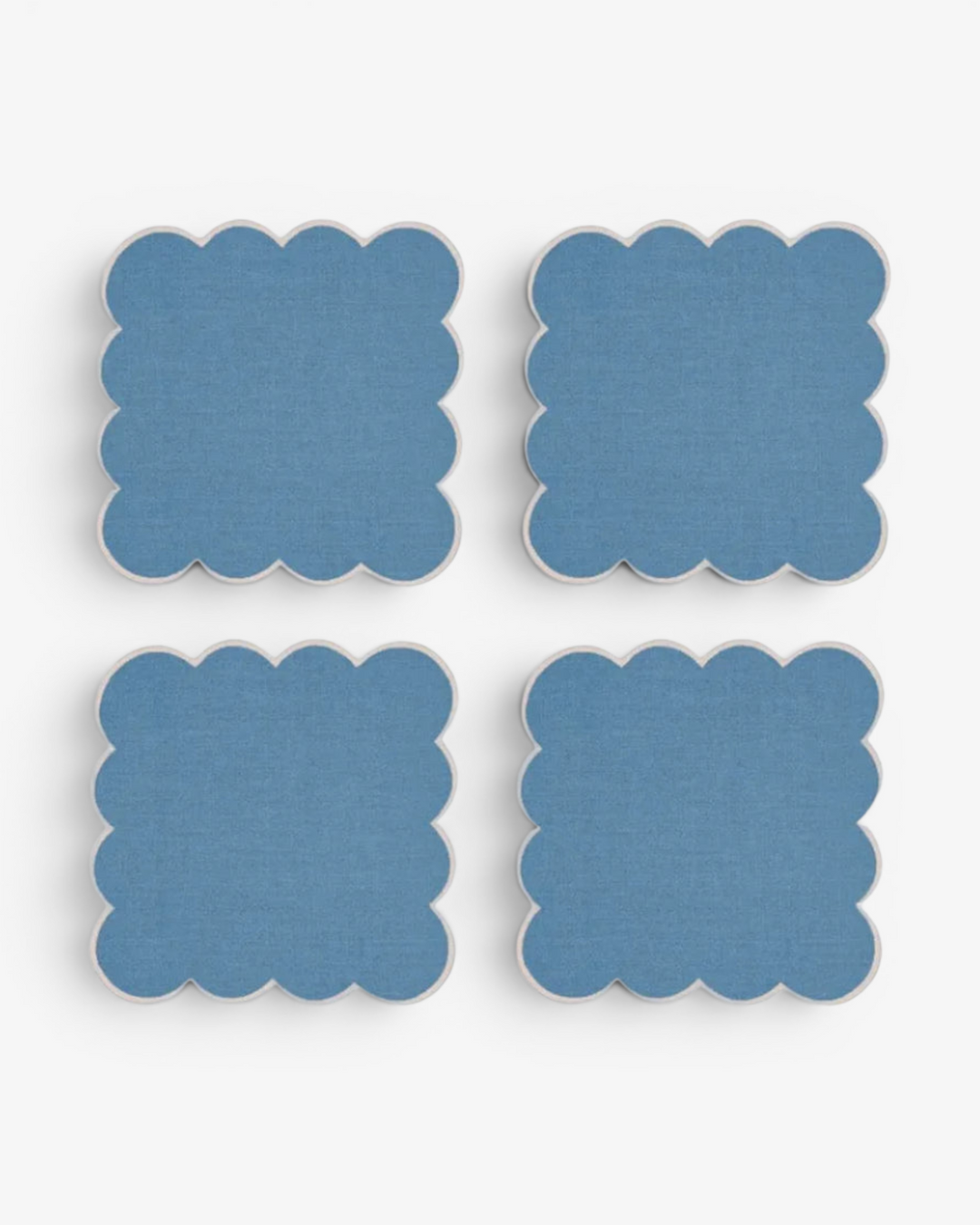 Four blue square coasters with scalloped edges on a white background