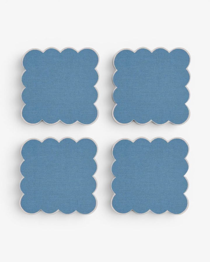 Four blue square coasters with scalloped edges on a white background