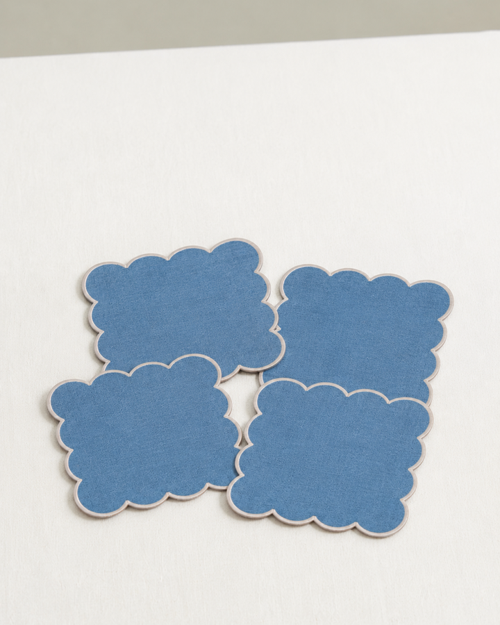 Four blue scalloped cocktail napkins on a white linen table cloth 