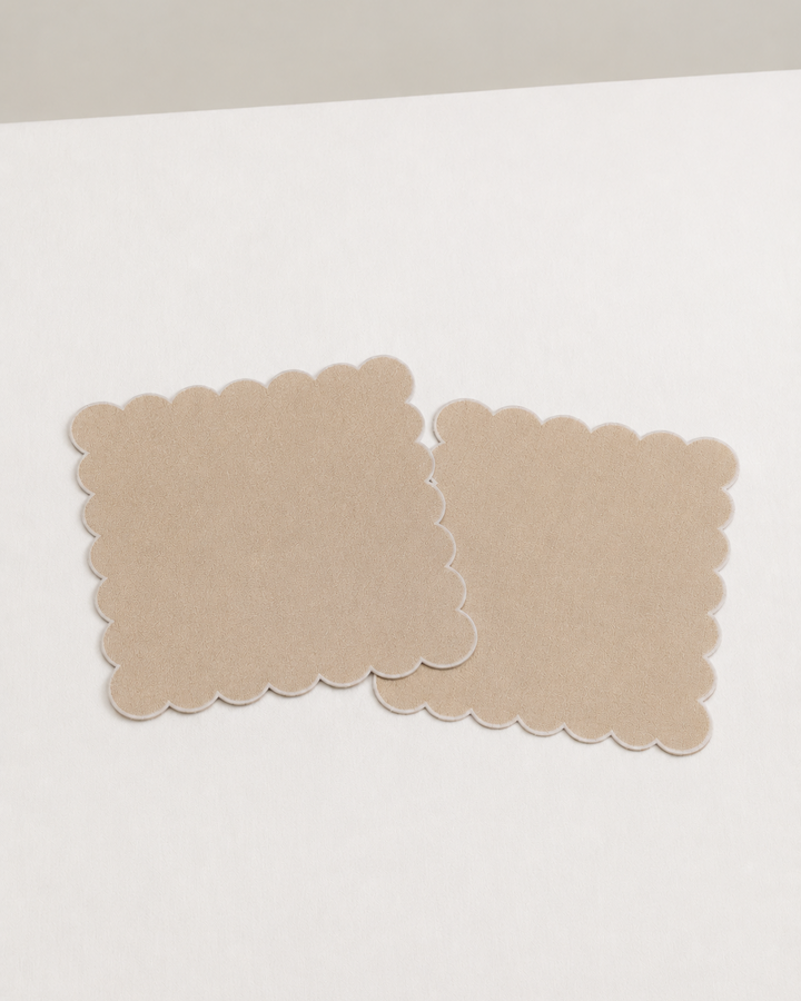 Two beige square napkins  with scalloped edges on a white surface.