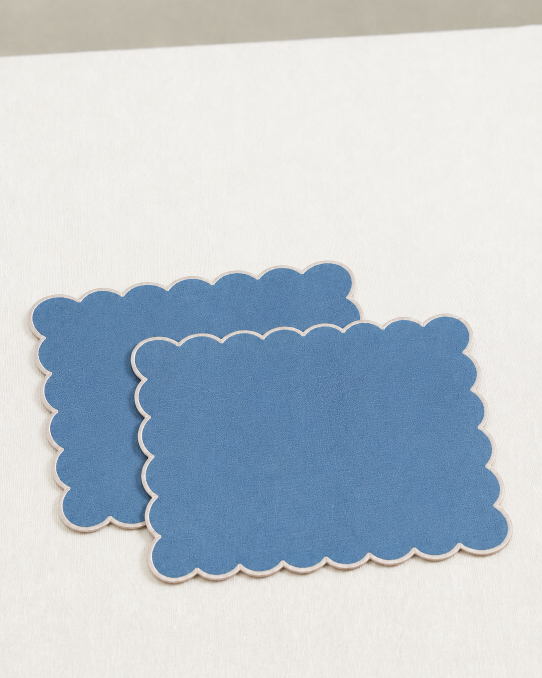 Two blue scalloped placemats on a white surface