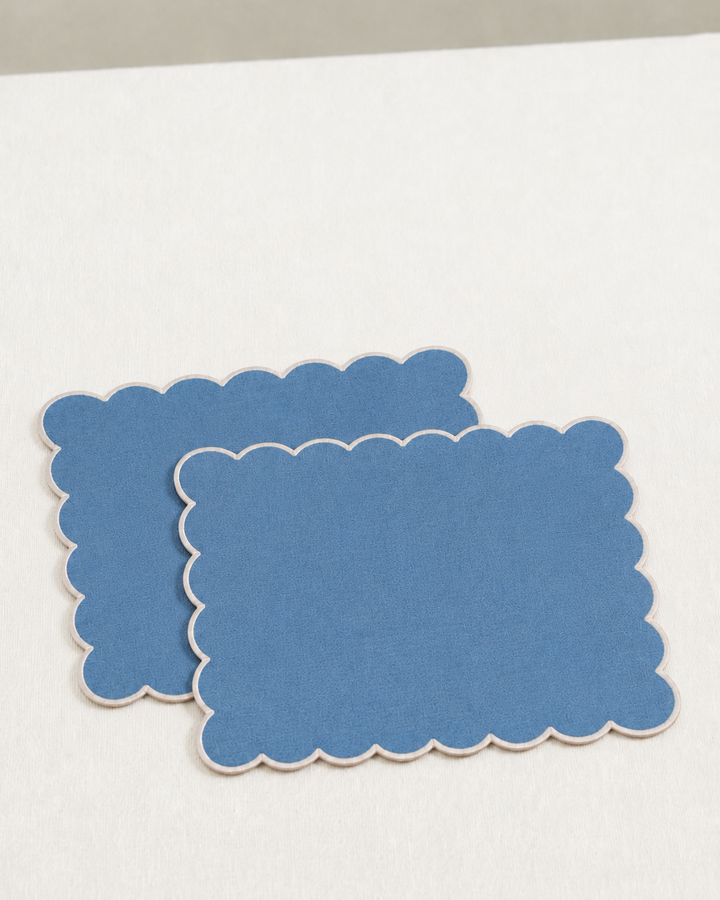 Two blue scalloped placemats on a white surface