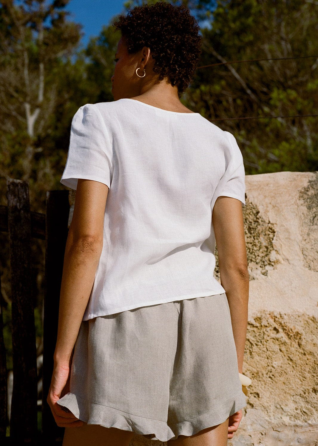 Person wearing a white top and beige shorts standing outdoors with trees in the background