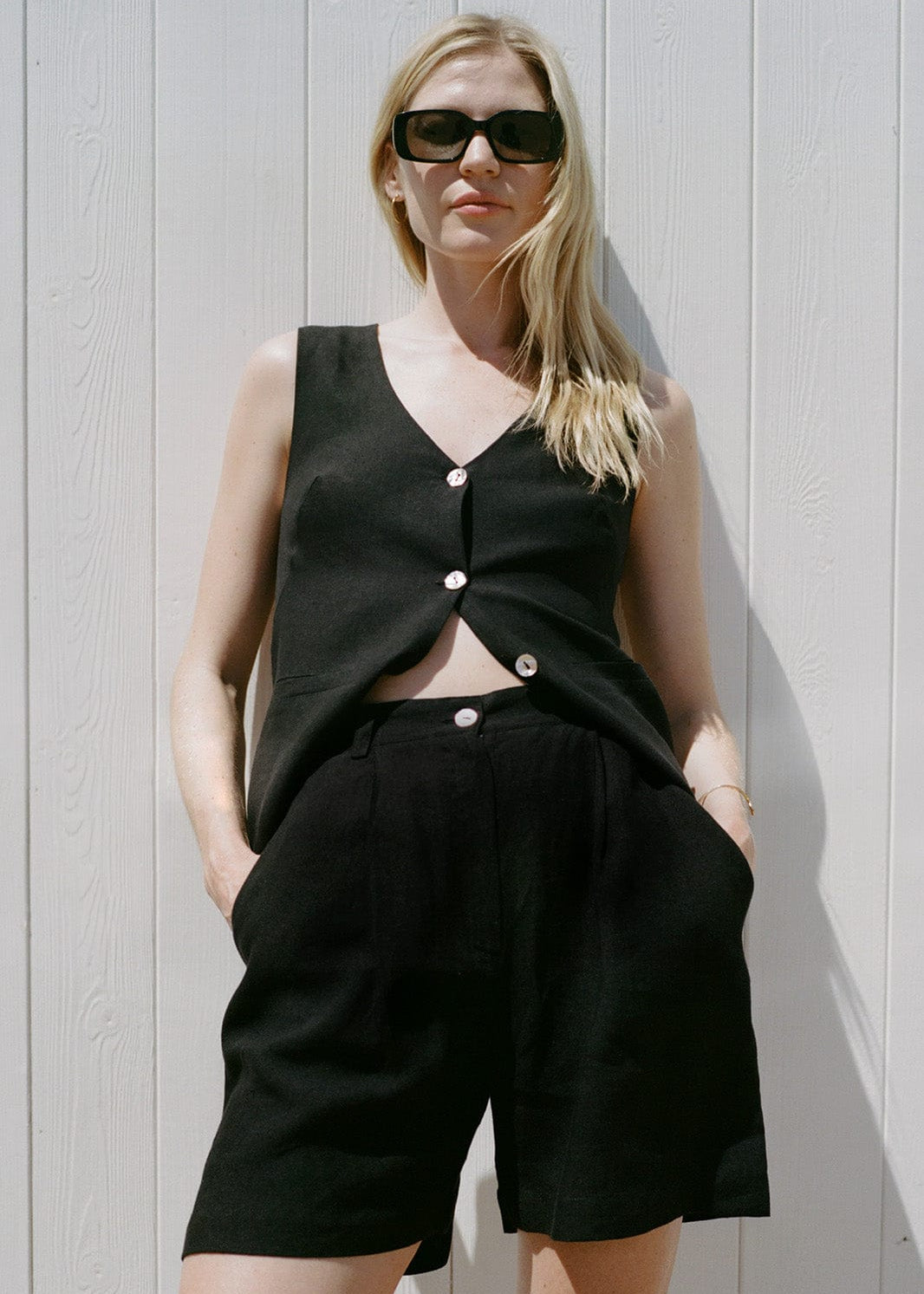 Woman wearing a black sleeveless top and shorts against a light wooden panel background