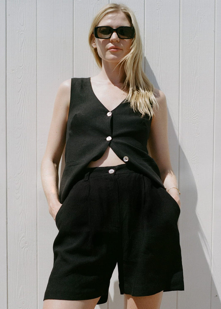 Woman wearing a black sleeveless top and shorts against a light wooden panel background