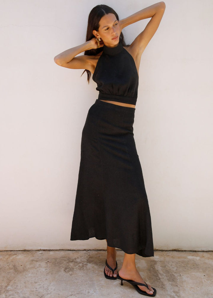 Woman wearing a black otop and skirt against a white wall