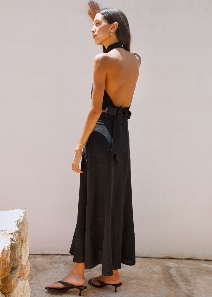 Woman wearing a black skirt and top with a backless design, standing against a neutral wall.