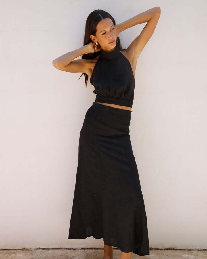 Woman wearing a black skirt and top against a white wall