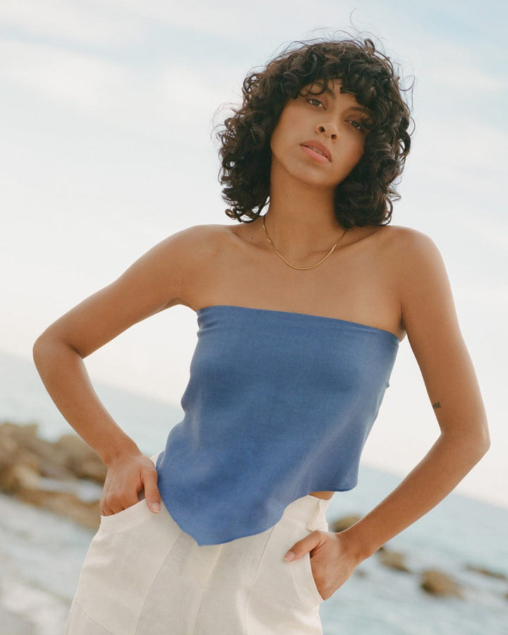 Woman wearing a blue strapless top and white pants standing on a beach.