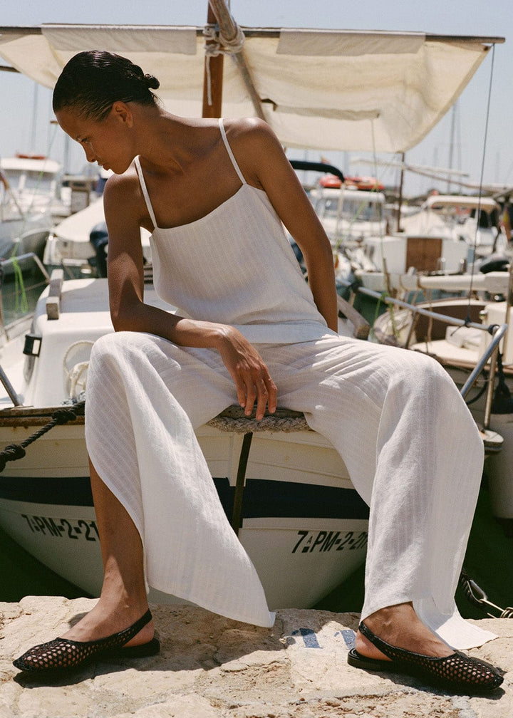 Woman in white outfit sitting on a boat dock with boats in the background
