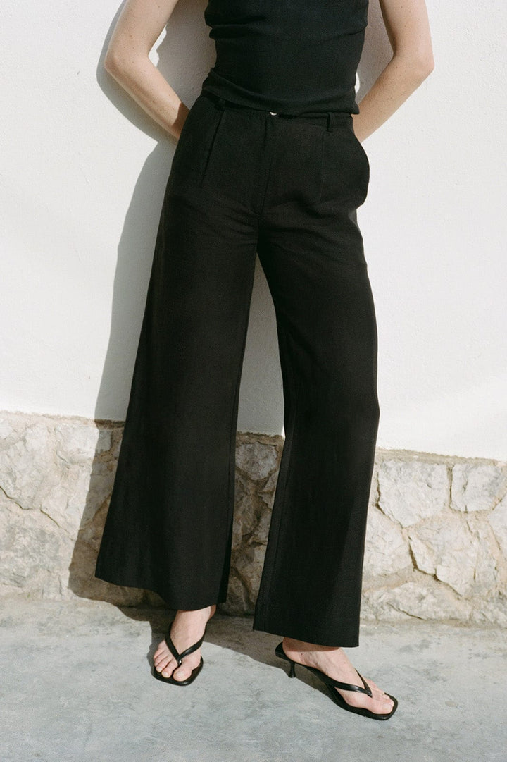 Person wearing black wide-leg pants against a light-colored wall.