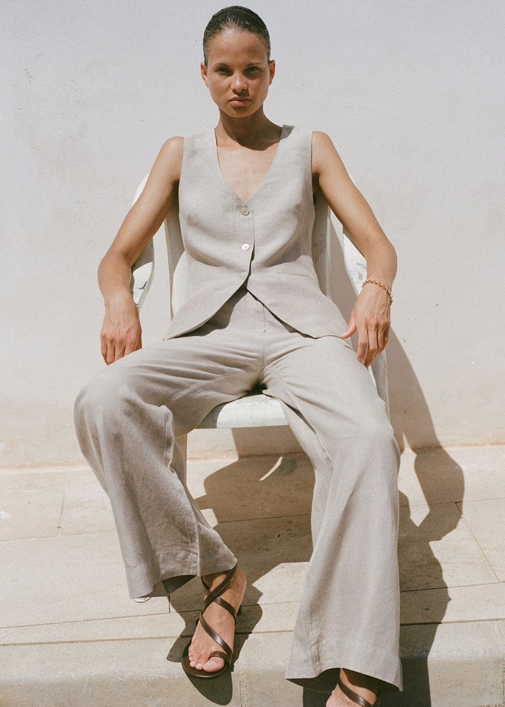 Woman wearing a beige sleeveless top and matching trousers sitting on a stone bench.