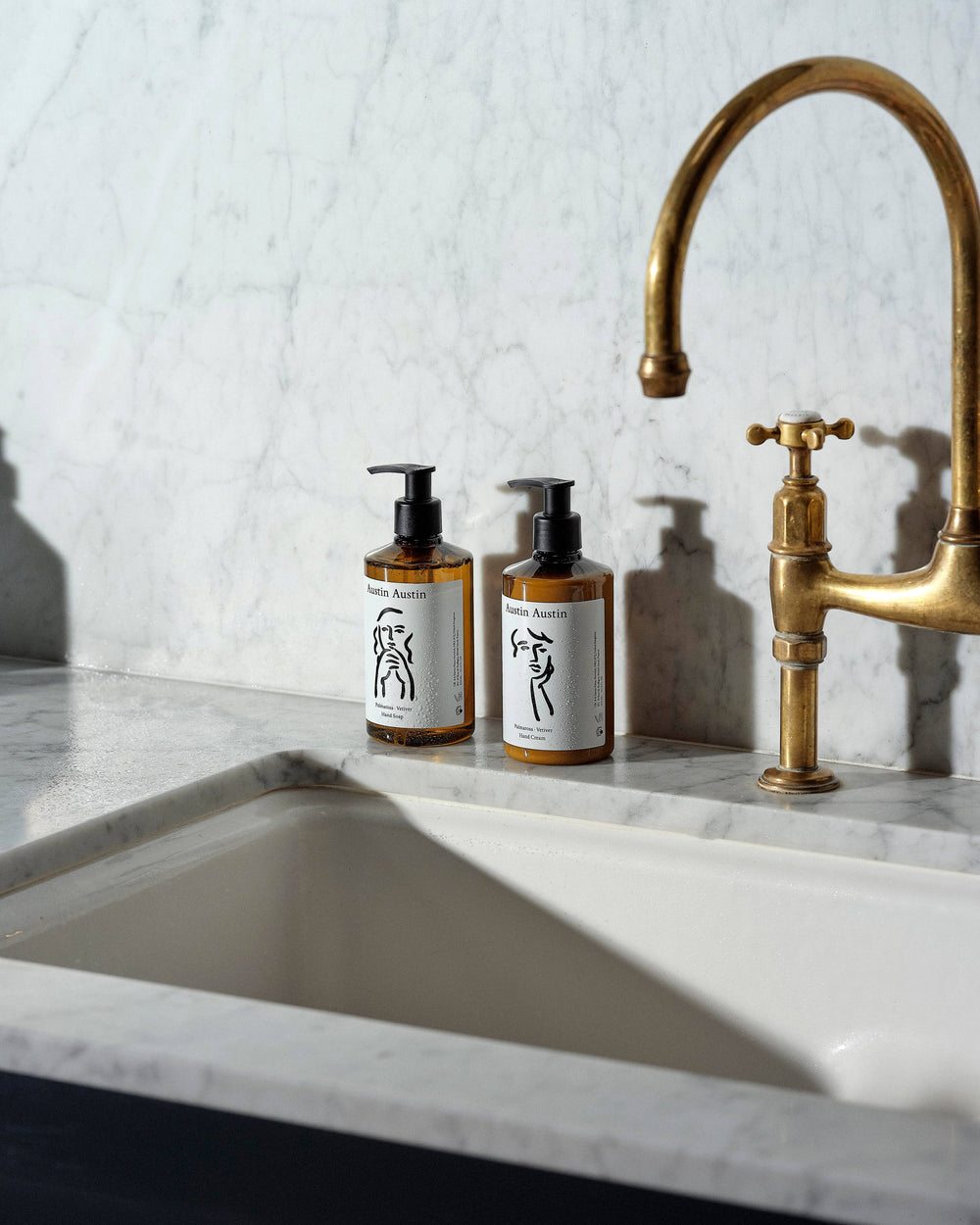 Two bottles of soap on a marble countertop with a gold faucet.