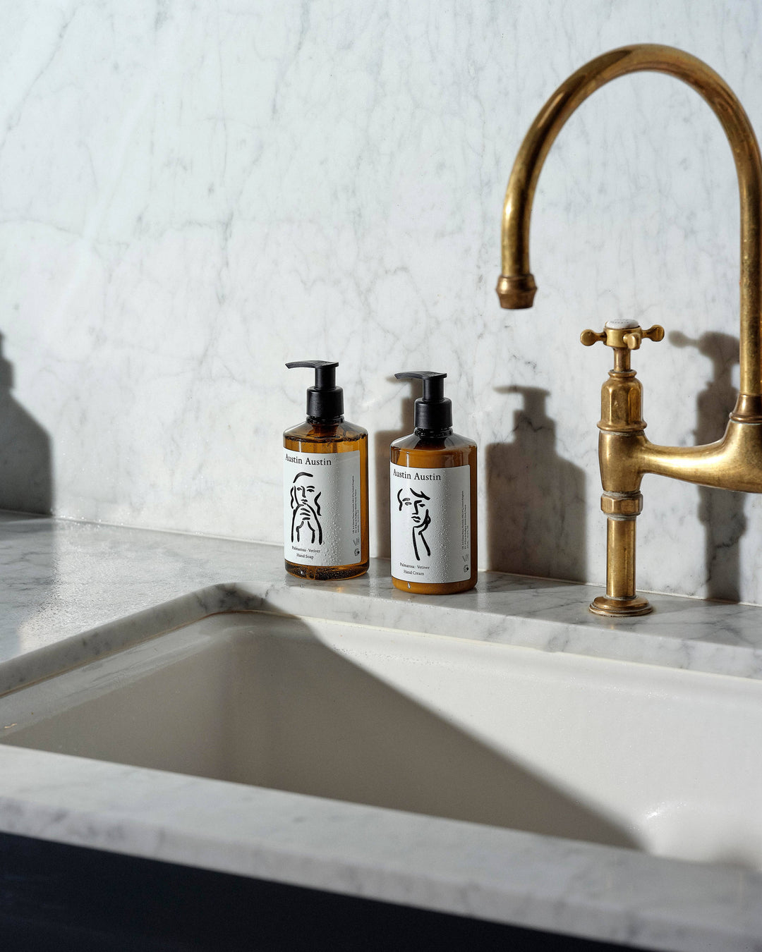 Two bottles of soap on a marble countertop with a gold faucet.