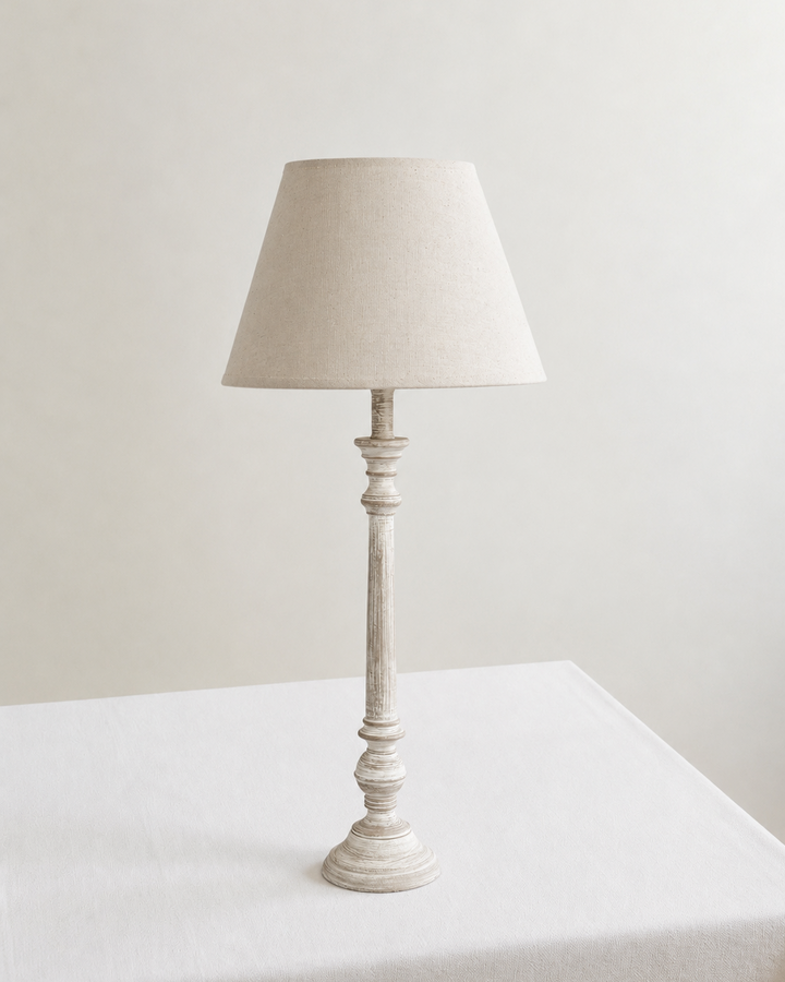 White table lamp with a beige lampshade on a white surface against a light gray background