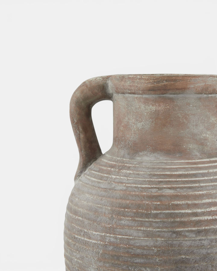 Close-up of a textured ceramic vase with a handle on a light gray background