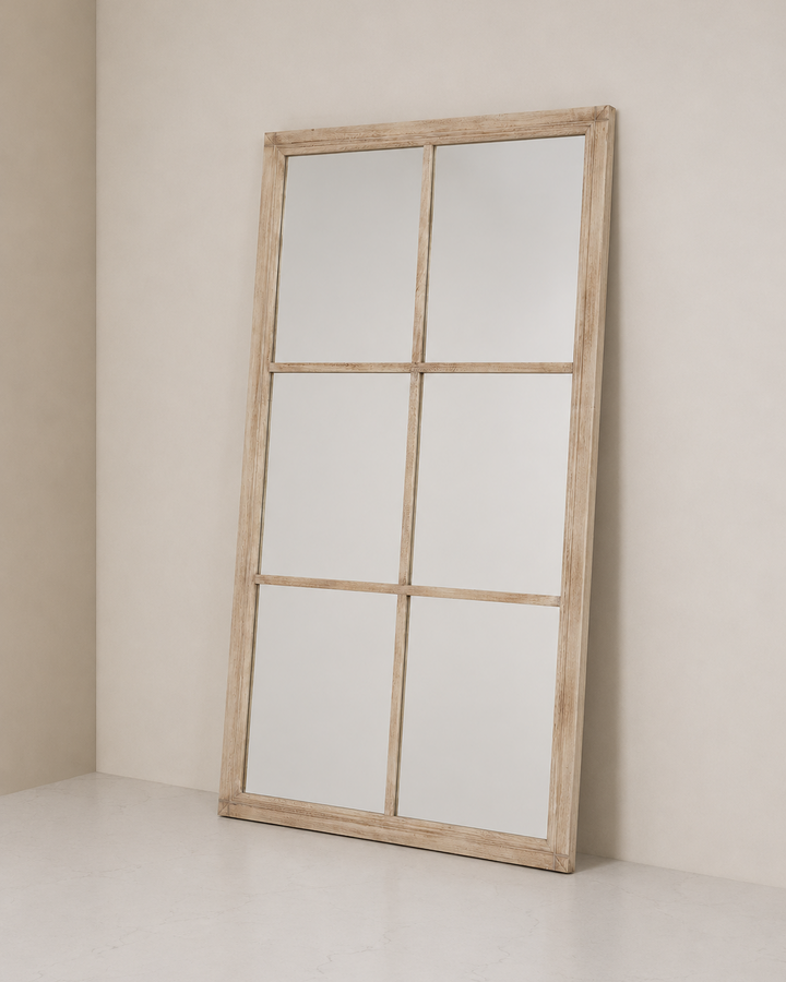 Large wooden-framed mirror leaning against a beige wall.