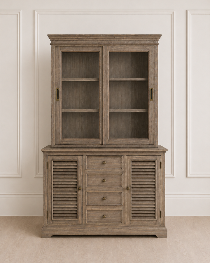 Wooden cabinet with glass doors and shutters on a beige floor and white paneled wall.
