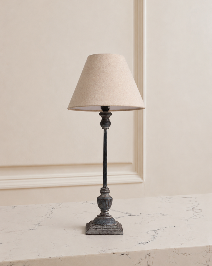 Table lamp with a beige shade on a marble surface against a neutral wall.