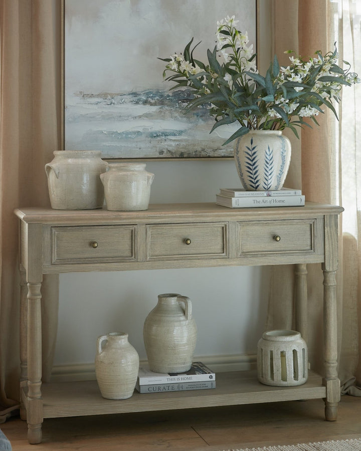Byretto Mercer console table in light wood with three drawers and an open lower shelf styled with ceramic vases.