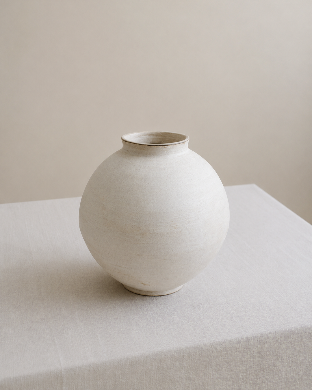 White ceramic vase on a white surface with a beige background