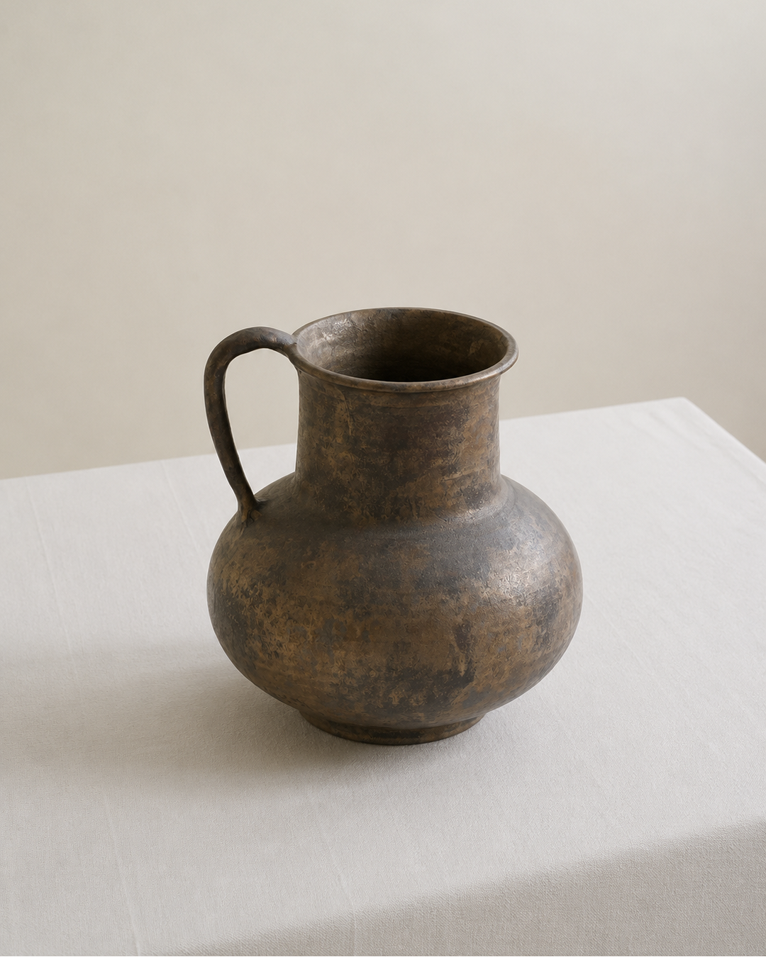 Bronze pitcher vase on a white surface with a beige background