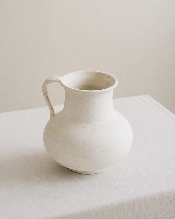 White ceramic pitcher vase on a light surface with a neutral background