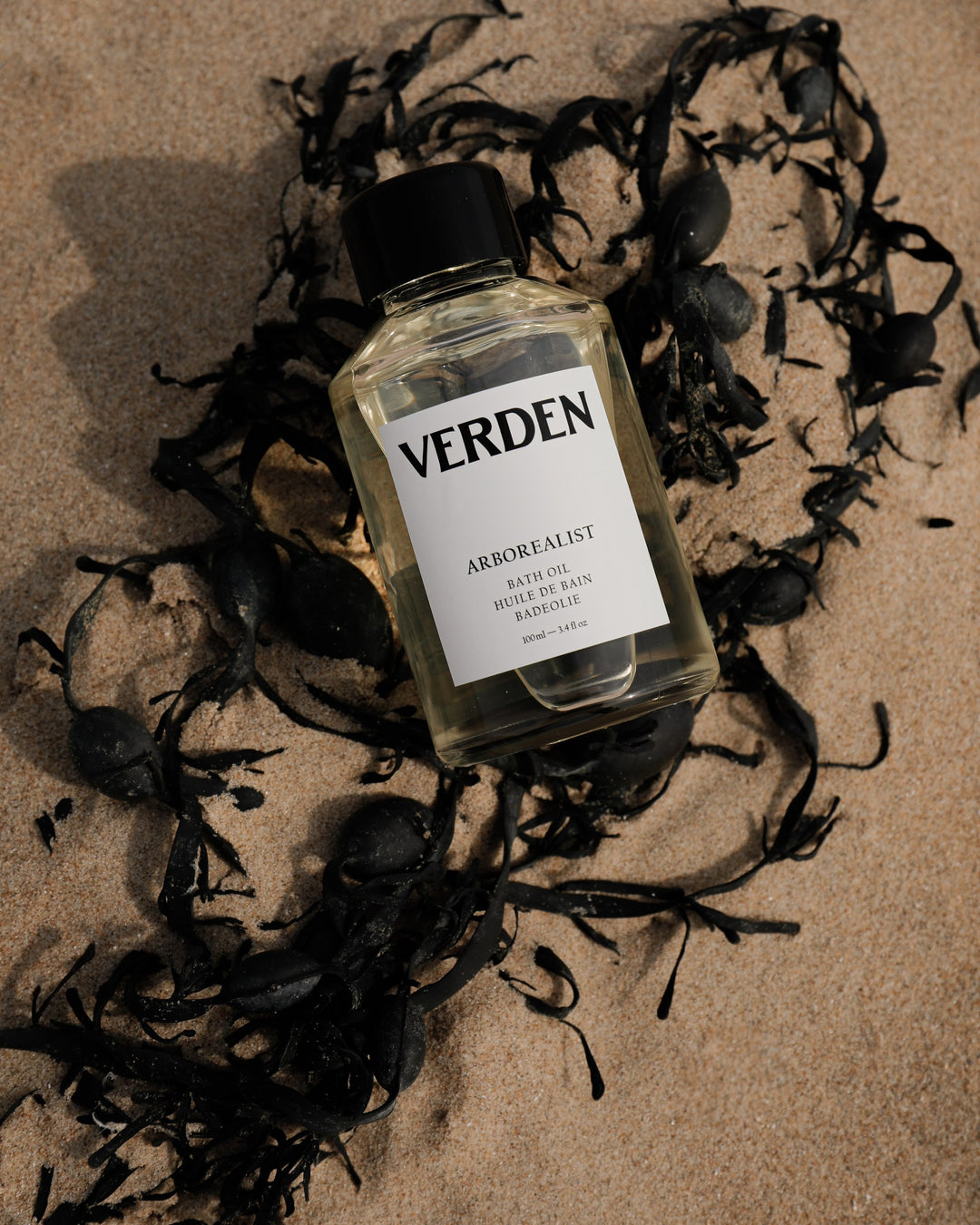 Bottle of Verden Arborealist Bath Oil surrounded by seaweed on a textured surface