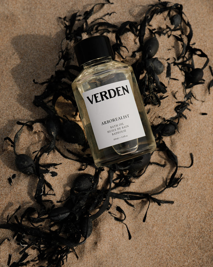 Bottle of Verden Arborealist Bath Oil surrounded by seaweed on a textured surface