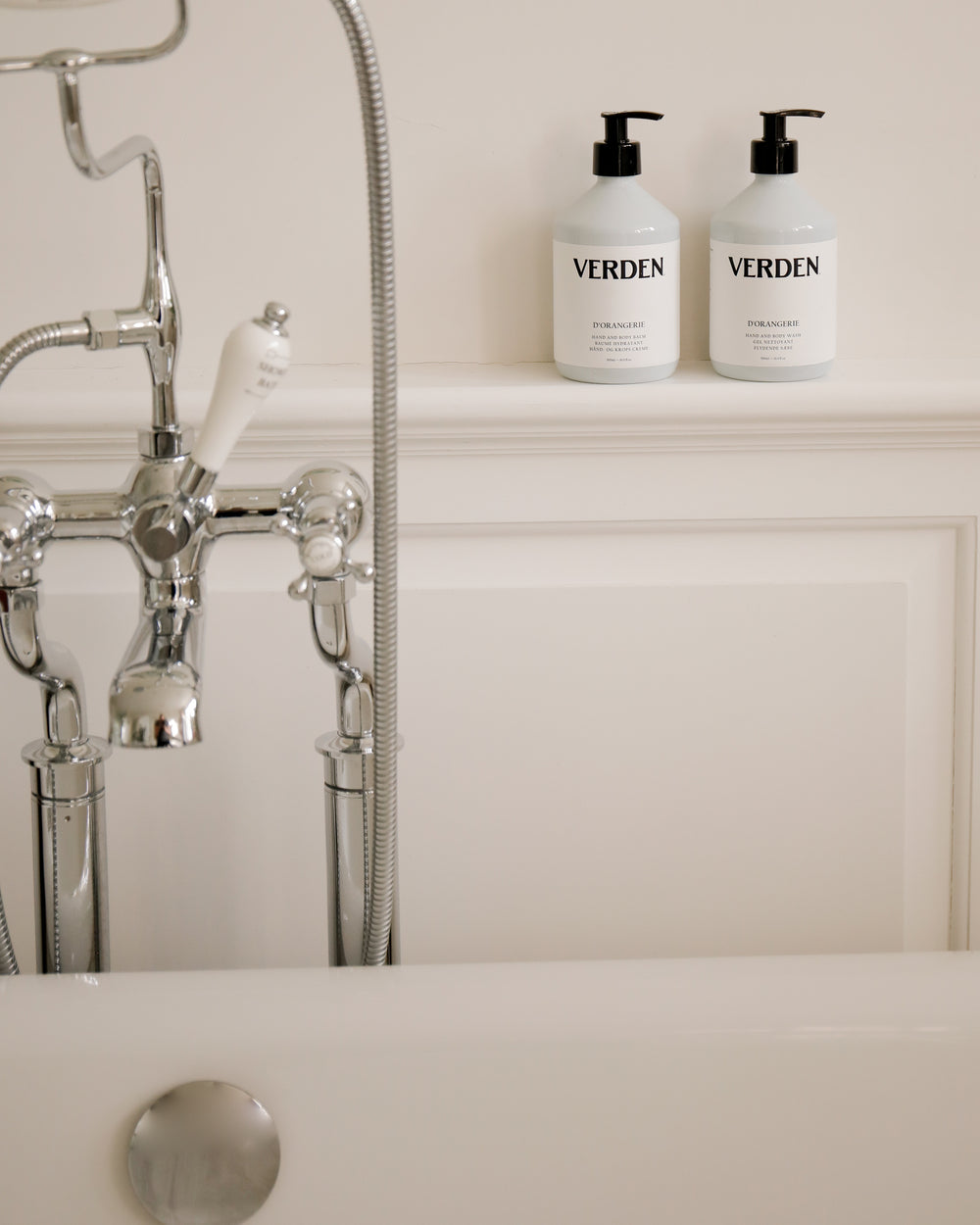 Two 'VERDEN' bottles on a bathroom shelf with a bathtub and faucet in the background.