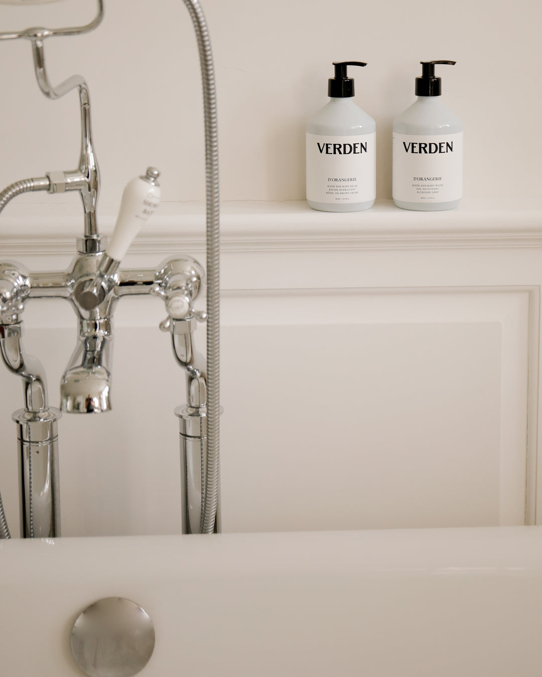 Two 'VERDEN' bottles on a bathroom shelf with a bathtub and faucet in the background.