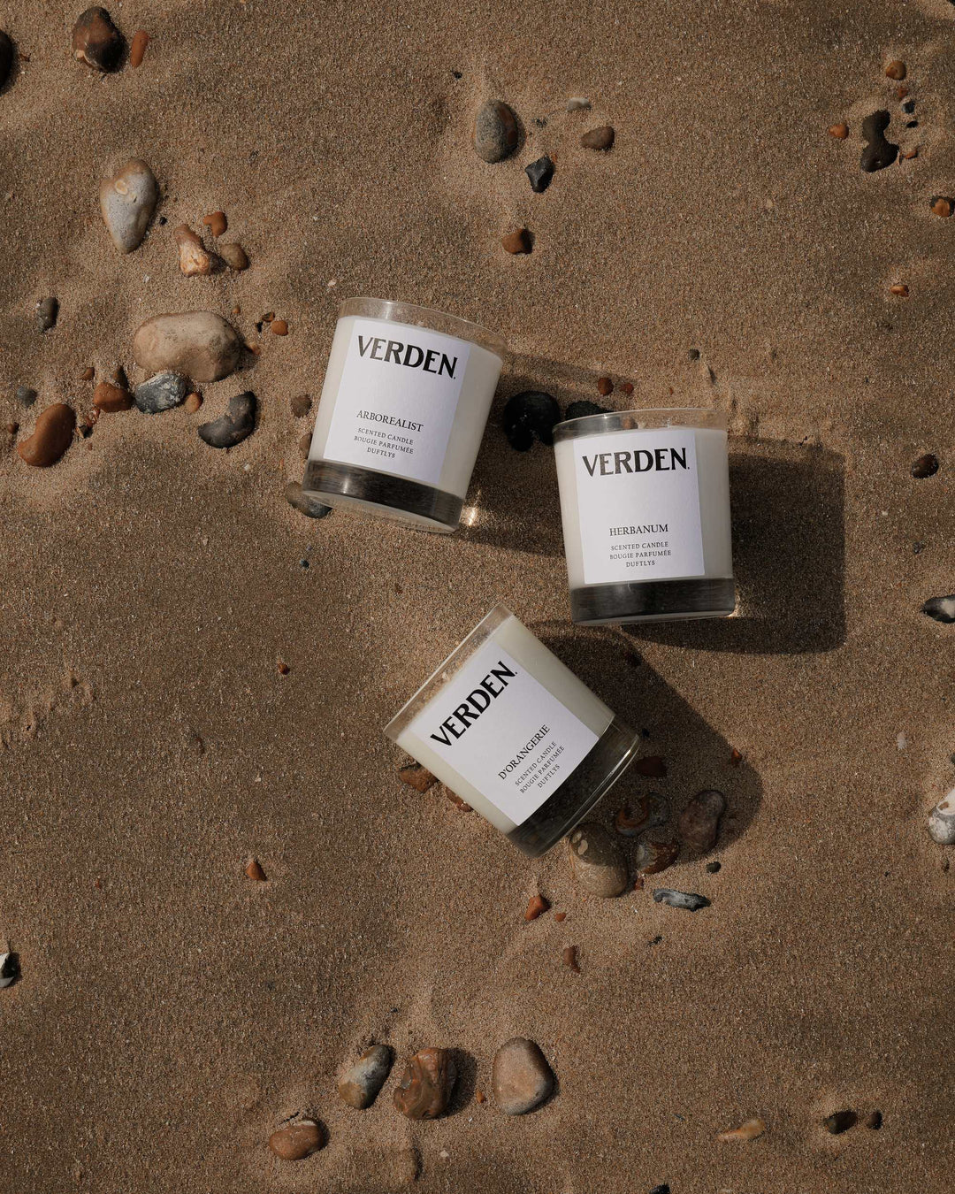 Three Verden candles on a sandy surface with rocks.