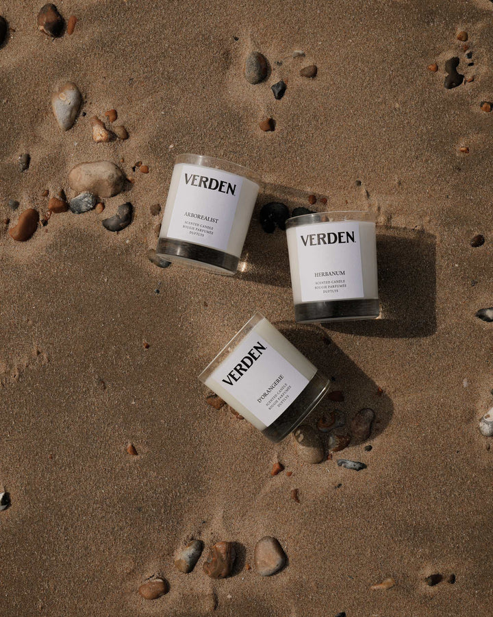 Three Verden candles on a sandy surface with rocks.