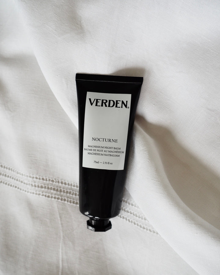 A black squeeze tube of VERDEN Nocturne hand cream resting on a draped white fabric background.