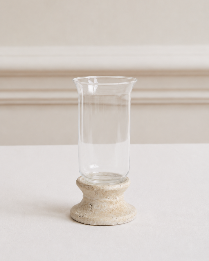 Clear glass candle holder with a textured stone base on a white surface