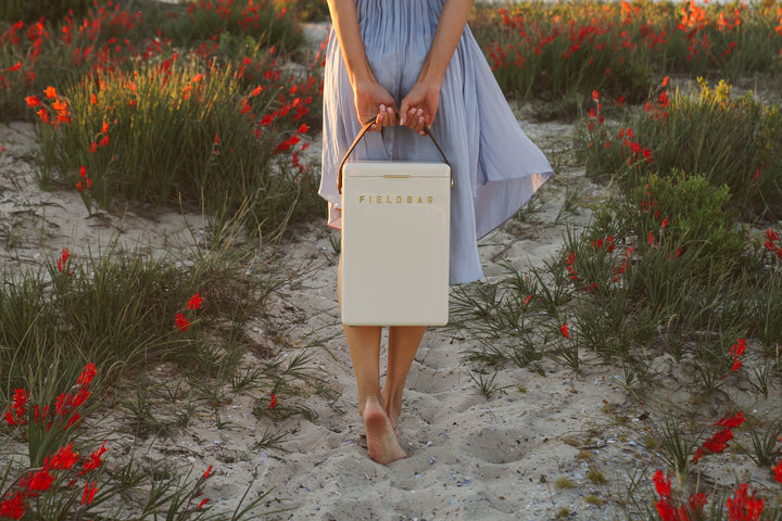 Person holding a white cooler with 'Fieldbar' branding in a field of red flowers.