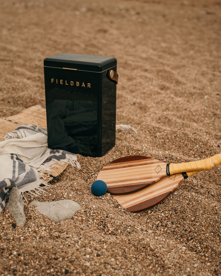 Black Fieldbar container with wooden paddles and a blue ball on sand