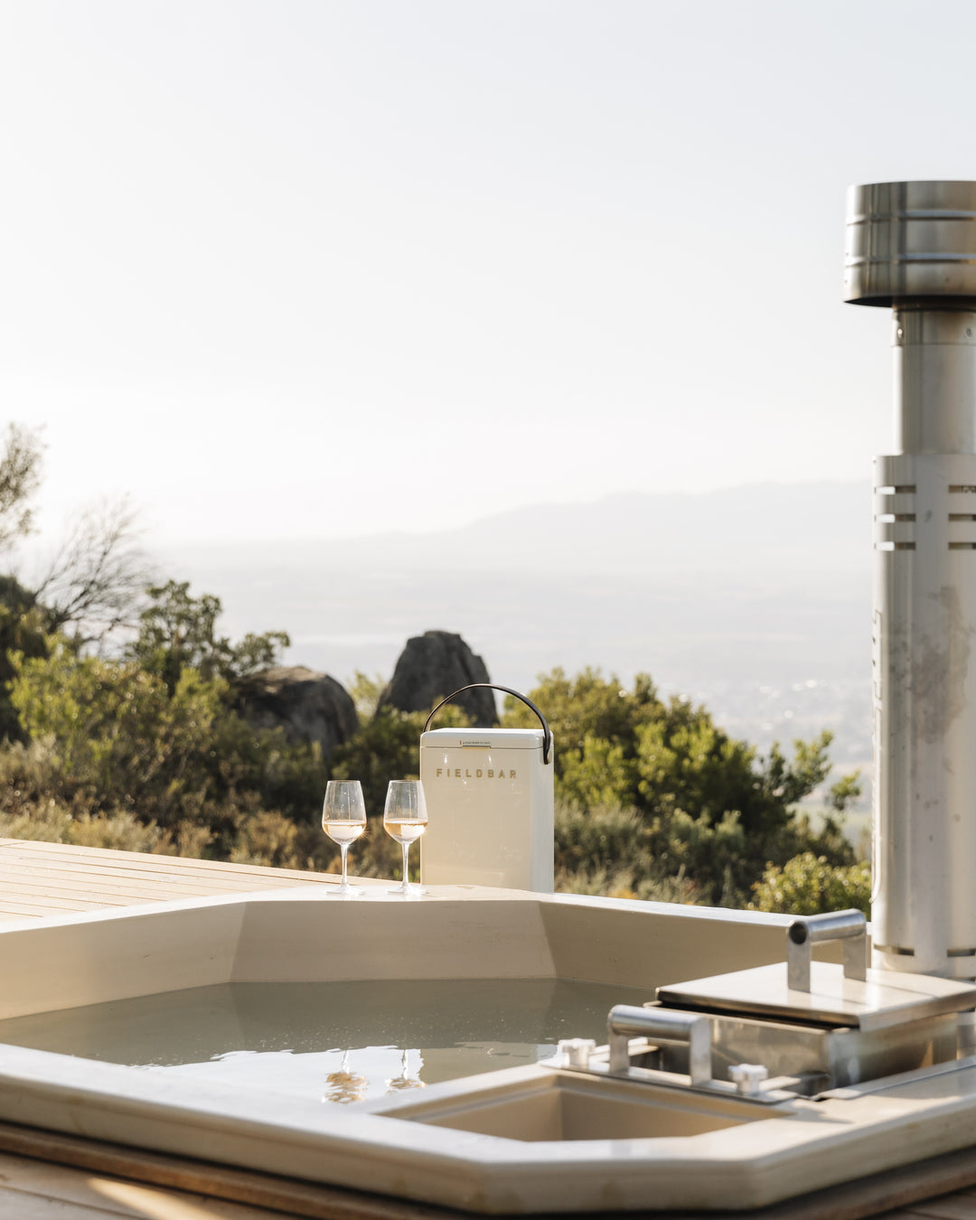 Outdoor hot tub with wine glasses and a fieldbar wine box cooler on a sunny day.
