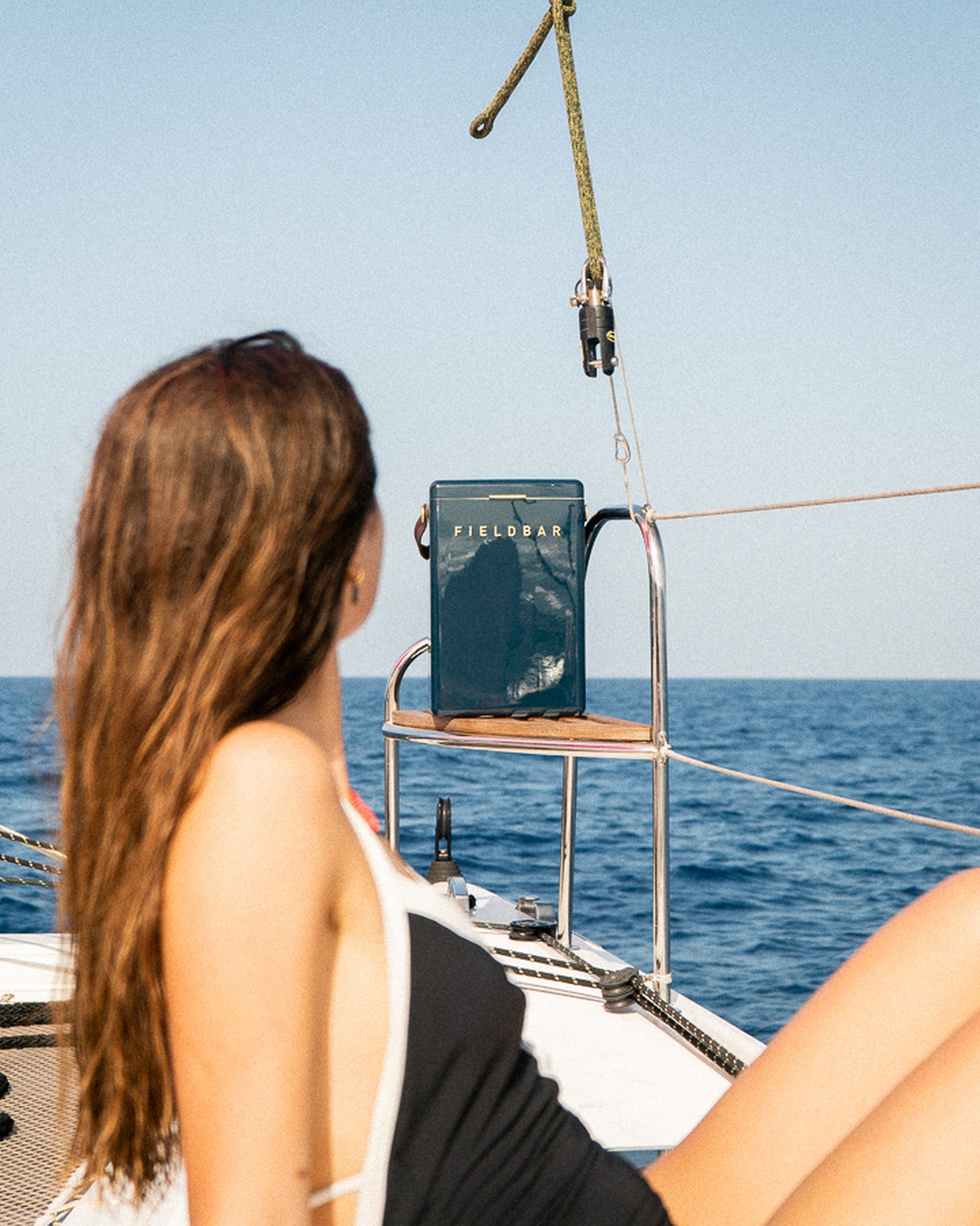 Woman on a sailboat holding a Fieldway mug with a clear blue sky and ocean background