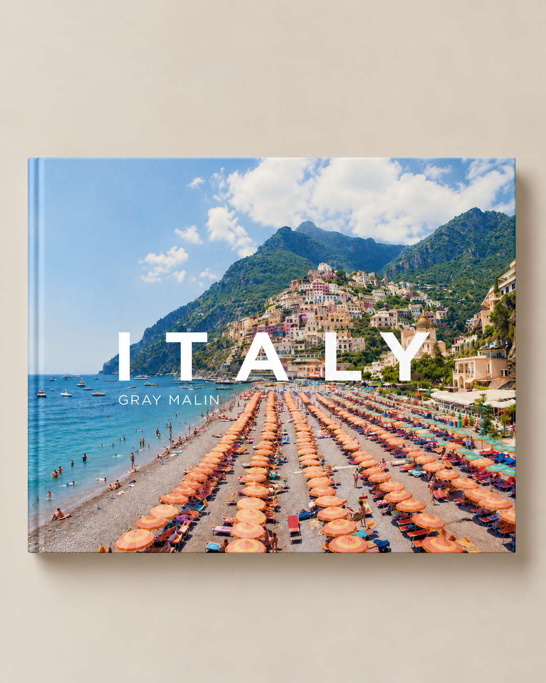 A hardcover book titled 'ITALY' by Gray Malin, featuring a large, vibrant beach photograph of Amalfi, Italy on the cover, displayed against a warm beige background.