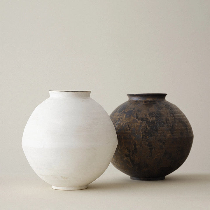 Two ceramic vases, one white and one black with gold, on a light background