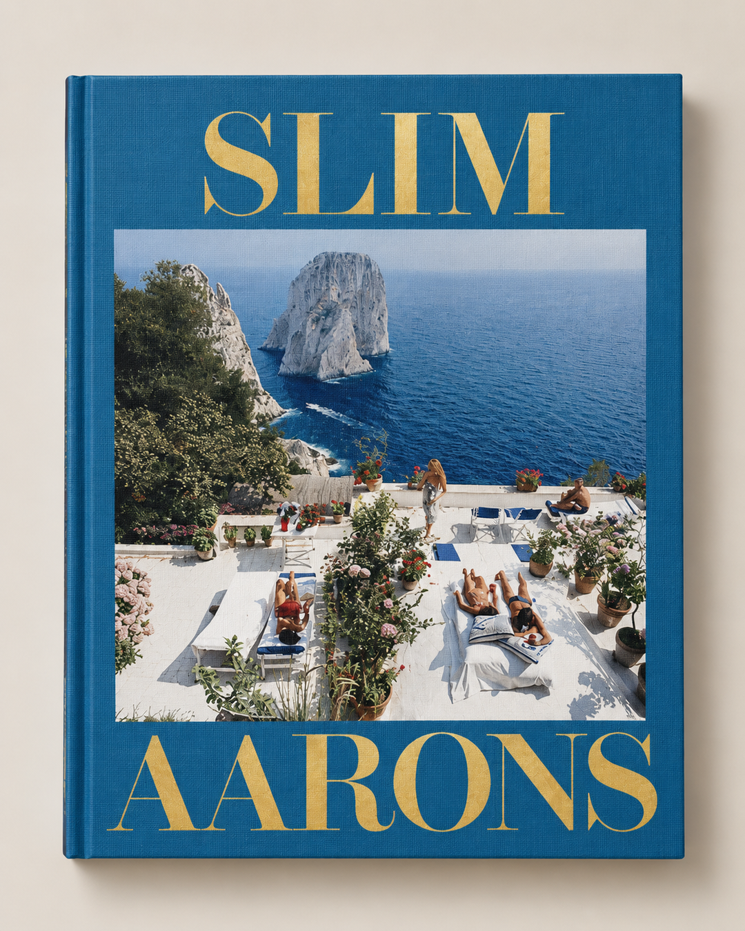 Slim Aarons travel guide book with a deep blue cover, gold lettering, and a central photograph of a coastal resort scene.